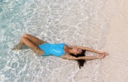 A woman relaxing on the beach enjoying her abdominoplasty results.