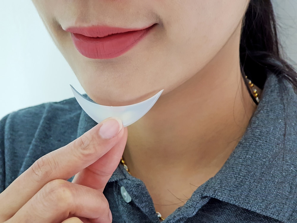 Woman holding a chin implant under her chin to visualize enhancement and assess facial symmetry improvement.