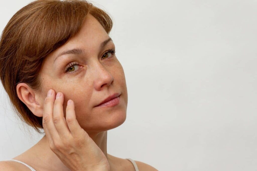 Thoughtful woman touching her cheek, assessing readiness for facelift following major weight loss and recovery