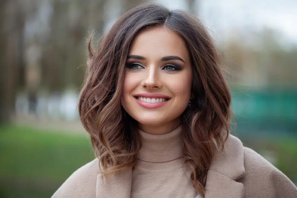 Confident brunette smiling outdoors after facial fat transfer, showing smooth, youthful volume retention