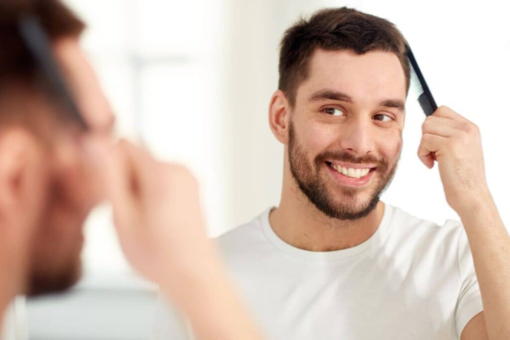 Happy man with healthy hair combing in mirror, showing results of Ariessence PDGF+ hair restoration treatment.