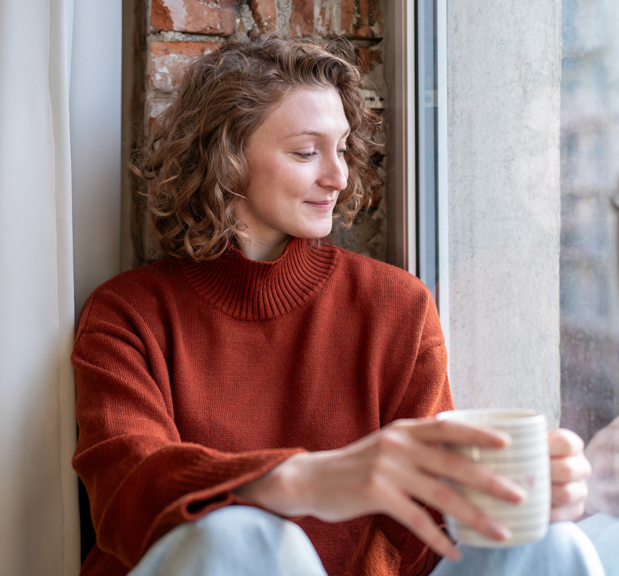 Woman relaxing by window with a warm drink, representing minimal downtime after biostimulant skin treatments