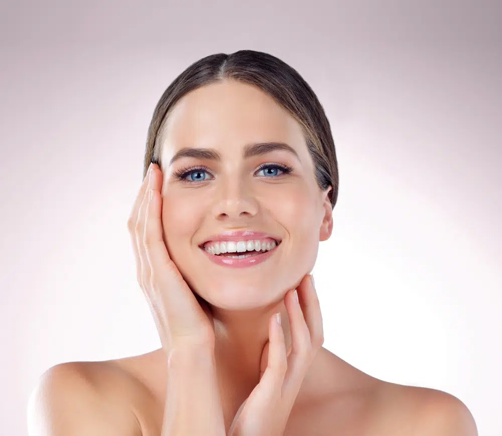 Smiling woman with clear skin touching face, representing PRF EZ Gel results and natural skin rejuvenation process